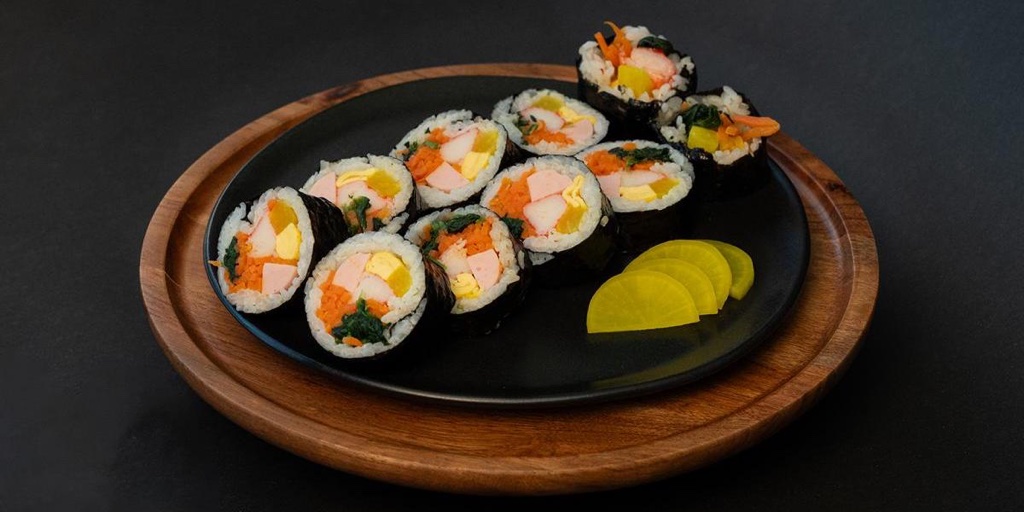 Official photograph of signature classic Appa's Kimbap sliced on dark plate with pickled radish